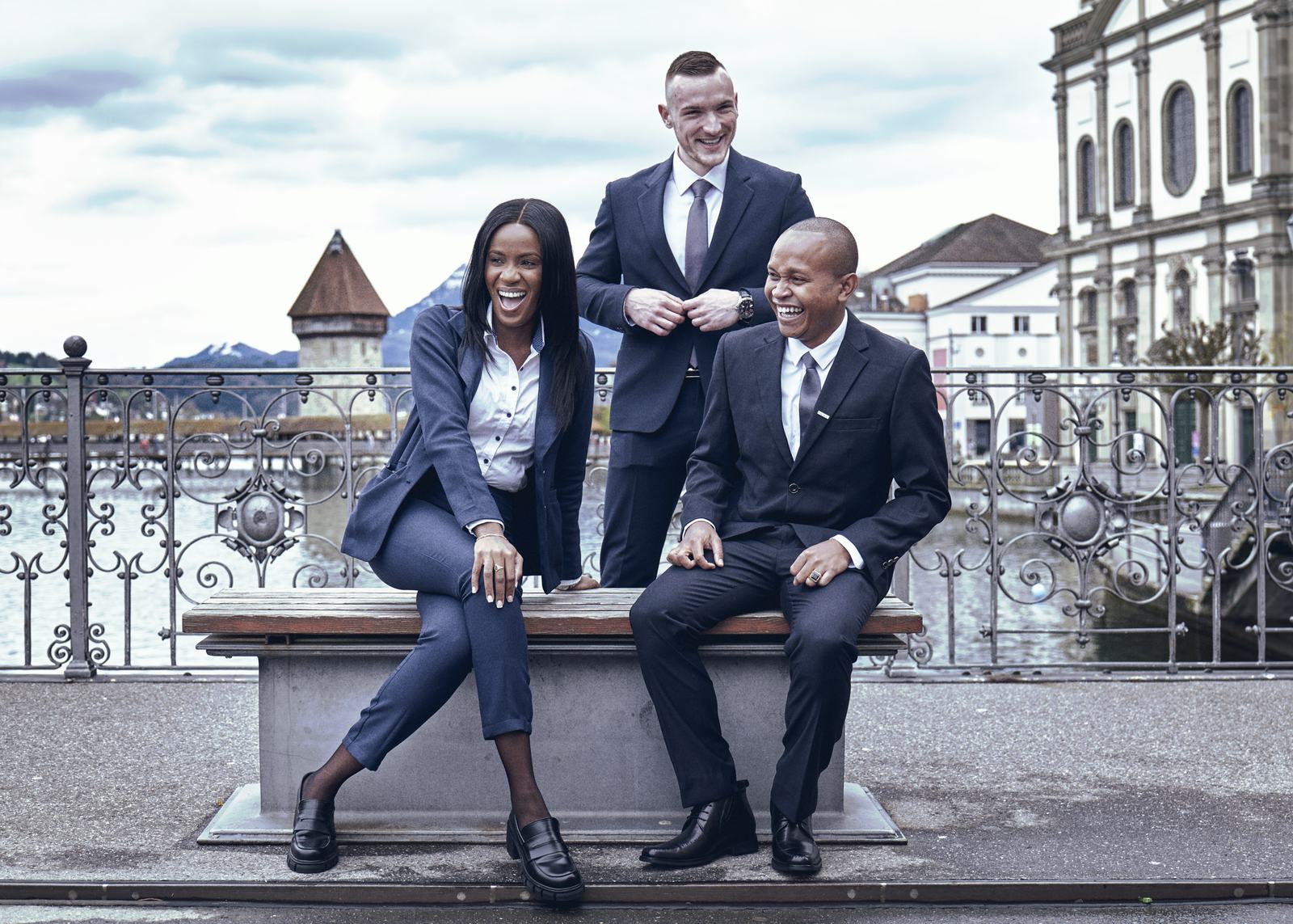 Three young BHMS students in business dress laughing on a bridge by the Lucerne waterfront